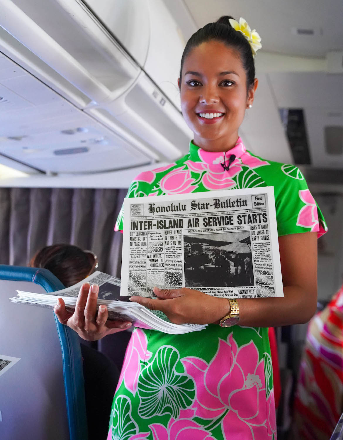A cabin crew member dressed in a vintage uniform hands out copies of a 11 November 1929 edition of the Honolulu Star-Bulletin.